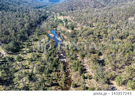 Aerial photograph of a winding river through forested hills, with rocky shallows, open clearings and native bushland across a remote rural valley. 143857243