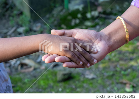 Adult woman holding a young child small hand gently outdoors in daylight. Caring family relationship, trust, protection, and emotional bond. Adult woman holding a young child small hand gently outdoors in daylight. Caring family relationship, trust, protection, and emotional bond. 143858602