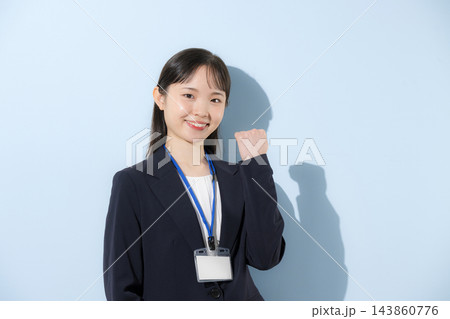 [水色背景]社員証を首から下げて立つスーツ姿の若い20代前半のような日本人女性、ガッツポーズ 143860776