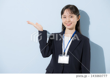 [水色背景]社員証を首から下げて立つスーツ姿の若い20代前半のような日本人女性こちら案内 143860777