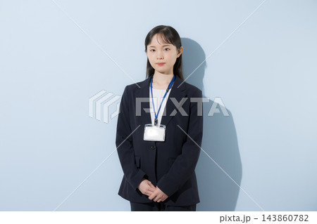 [水色背景]社員証を首から下げて立つスーツ姿の若い20代前半のような日本人女性、真剣で真面目な表情 143860782