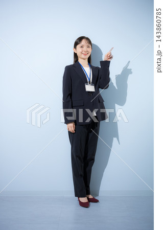 [水色背景]社員証を首から下げて立つスーツ姿の若い20代前半のような日本人女性　指差し 143860785