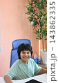 Cheerful boy seated at desk smiles directly toward viewer in calm office. Young child looks at ease in blue chair, conveying reassurance and welcoming family support environment, while facing forward. 143862335