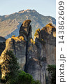 Meteora Greece massive rock pillars glowing in sunset light behind green trees 143862609