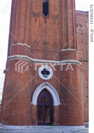 Red brick tower facade, featuring arch doorway with white trim and cross design 143862678