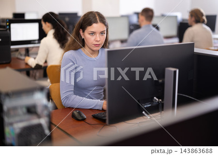 Young woman student of computer courses looks at monitor screen, types on keyboard and does work Young woman student of computer courses looks at monitor screen, types on keyboard and does work 143863688