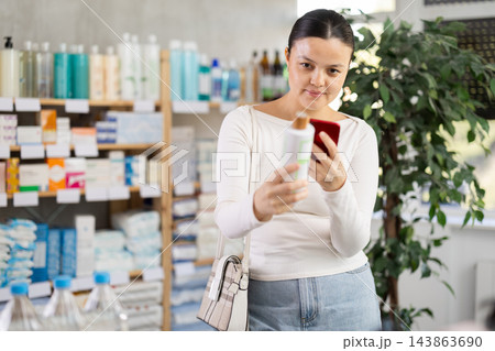 Middle-aged woman scanning QR-code on shampoo or gel in drugstore 143863690
