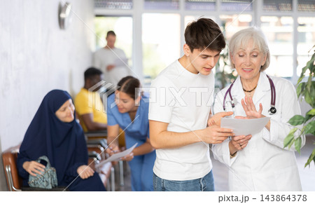 Smiling elderly female doctor showing papers to guy 143864378