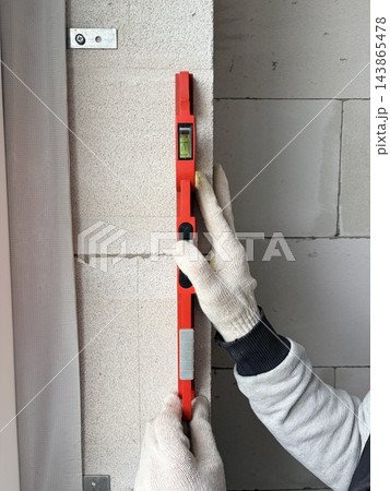 A builder checks the level of an aerated concrete wall using a spirit level. Construction and renovation concept A builder checks the level of an aerated concrete wall using a spirit level. Construction and renovation concept 143865478
