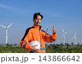 Confident wind farm technician showing thumbs up while holding safety helmet at renewable energy turbine field 143866642