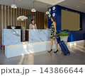 Modern hotel lobby with marble reception desk. Female guest checking in with suitcase while uniformed receptionist assists. 143866644