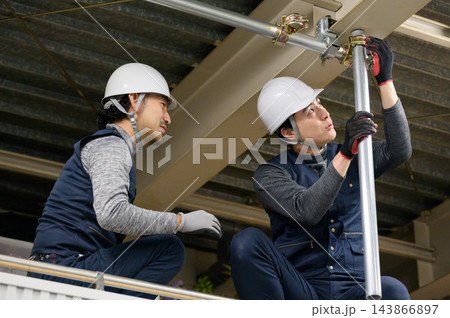 屋内の建設現場で協力して足場の単管パイプを組み立てる男性作業員2人 143866897