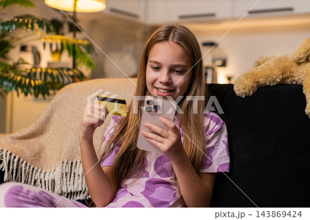 Teenager girl uses smartphone with credit card chooses book or toy online happy mood ready to buy Teenager girl uses smartphone with credit card chooses book or toy online happy mood ready to buy 143869424