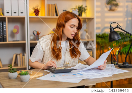 Young woman on home table paying bills with calculator and checking receipts during home budget task Young woman on home table paying bills with calculator and checking receipts during home budget task 143869446