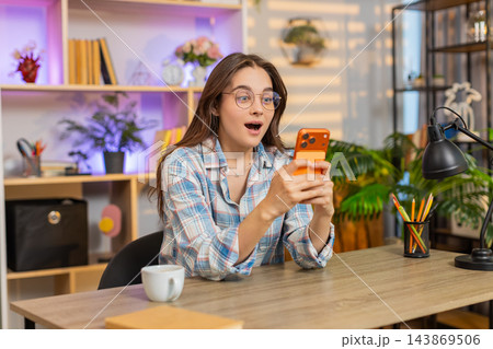 Young woman on home table reading smartphone good news feeling surprise joy luck and success indoors 143869506