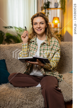 Young woman on home sofa writing personal goals in notebook smiling with inspiration and check mark Young woman on home sofa writing personal goals in notebook smiling with inspiration and check mark 143869528