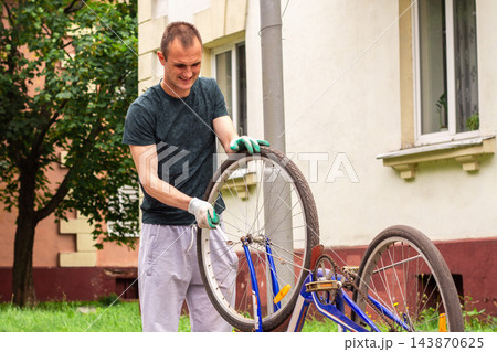Man examining bike chain and gears for wear. Upside down position reveals issues. Practical competence outside house Man examining bike chain and gears for wear. Upside down position reveals issues. Practical competence outside house 143870625
