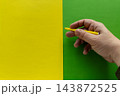 Hand Holding Yellow Pen Over Split Yellow And Green Paper Background For Design And Writing 143872525