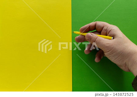 Hand Holding Yellow Pen Over Split Yellow And Green Paper Background For Design And Writing Hand Holding Yellow Pen Over Split Yellow And Green Paper Background For Design And Writing 143872525