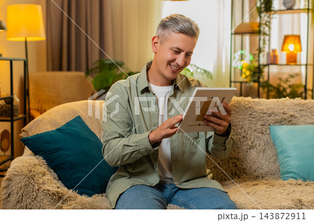 Middle-aged man on home sofa holds framed old photo smiles softly and recalls warm family memories 143872911