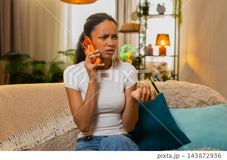 African American young woman on home sofa calling bank support to explain bank card payment problem African American young woman on home sofa calling bank support to explain bank card payment problem 143872936