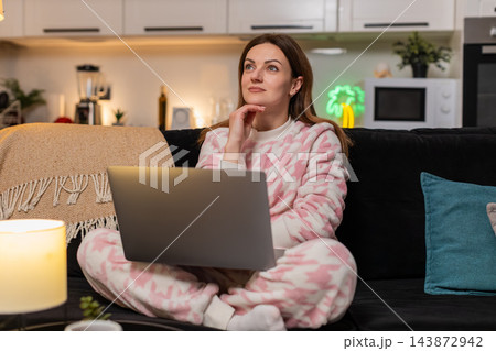 Adult woman with laptop at night deep in thought during remote work online session focused calm deep 143872942