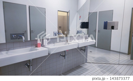 Clean public restroom with multiple sinks, mirrors and toilet cubicles in a modern facility. Concepts: public hygiene, sanitation infrastructure, commercial interiors, facility maintenance Clean public restroom with multiple sinks, mirrors and toilet cubicles in a modern facility. Concepts: public hygiene, sanitation infrastructure, commercial interiors, facility maintenance 143873377