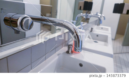 Clean public restroom with multiple sinks, mirrors and toilet cubicles in a modern facility. Concepts: public hygiene, sanitation infrastructure, commercial interiors, facility maintenance Clean public restroom with multiple sinks, mirrors and toilet cubicles in a modern facility. Concepts: public hygiene, sanitation infrastructure, commercial interiors, facility maintenance 143873379