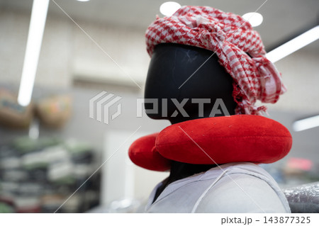 Traveler mannequin wearing a red U-shaped neck pillow and traditional headscarf inside an Egyptian market. Travel comfort tourism shopping and local trade Traveler mannequin wearing a red U-shaped neck pillow and traditional headscarf inside an Egyptian market. Travel comfort tourism shopping and local trade 143877325