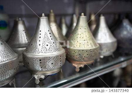Assortment of perforated metal lanterns displayed on a retail shelf in Egypt. Decorative lighting local trade and tourism shopping Assortment of perforated metal lanterns displayed on a retail shelf in Egypt. Decorative lighting local trade and tourism shopping 143877340