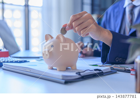 Businessman putting coin into piggy bank on office desk. Concept of saving money. 143877781