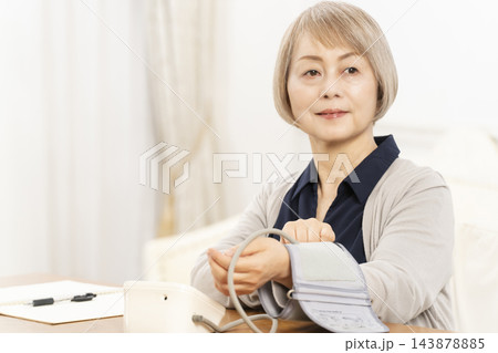 リビングで血圧を測り笑顔のシニア女性 143878885
