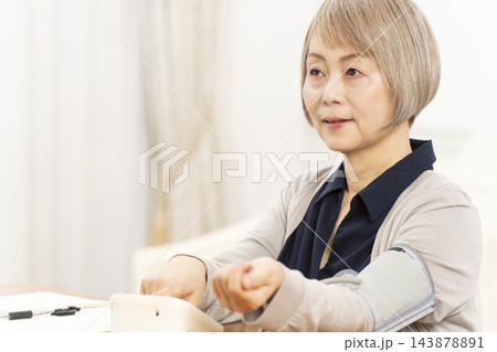 リビングで血圧を測り笑顔のシニア女性 143878891