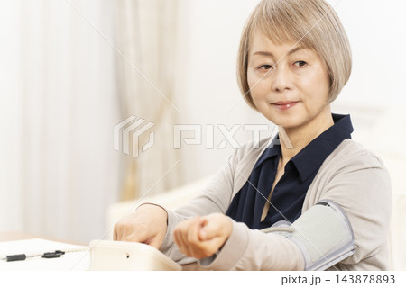 リビングで血圧を測り笑顔のシニア女性 リビングで血圧を測り笑顔のシニア女性 143878893