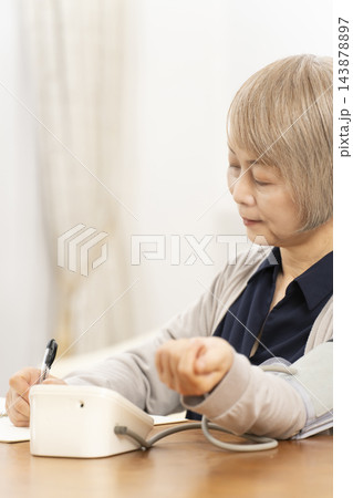 リビングで血圧を測り笑顔のシニア女性 リビングで血圧を測り笑顔のシニア女性 143878897