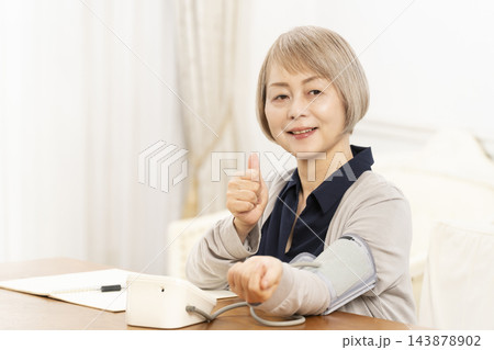 リビングで血圧を測り笑顔のシニア女性 143878902