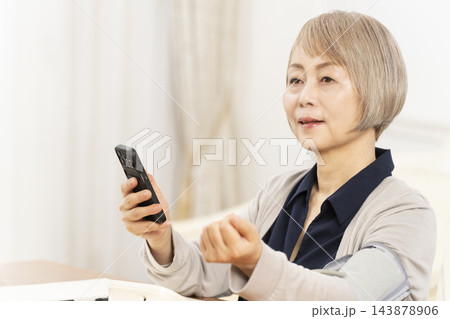 リビングで血圧を測り笑顔のシニア女性 143878906
