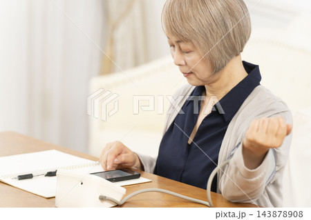 リビングで血圧を測り笑顔のシニア女性 143878908
