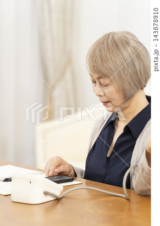 リビングで血圧を測り笑顔のシニア女性 143878910