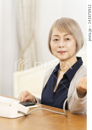 リビングで血圧を測り笑顔のシニア女性 リビングで血圧を測り笑顔のシニア女性 143878912