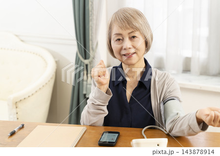 リビングで血圧を測り笑顔のシニア女性 143878914