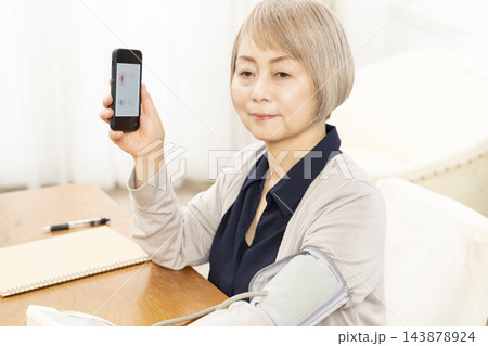 リビングで血圧を測り笑顔のシニア女性 リビングで血圧を測り笑顔のシニア女性 143878924