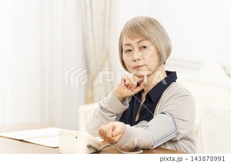リビングで血圧を測り落ち込むシニア女性 リビングで血圧を測り落ち込むシニア女性 143878991