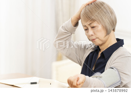 リビングで血圧を測り落ち込むシニア女性 リビングで血圧を測り落ち込むシニア女性 143878992
