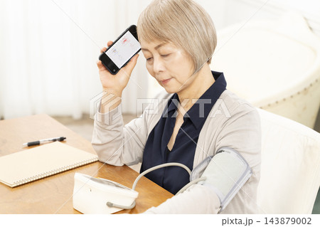 リビングで血圧を測り落ち込むシニア女性 143879002