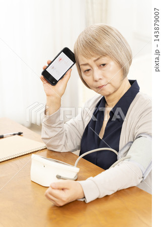 リビングで血圧を測り落ち込むシニア女性 143879007