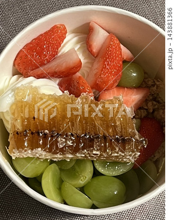 Swirled yogurt ice cream dessert served in a cup, smooth creamy texture with glossy surface, topped with fresh fruit pieces, highlighting its refreshing and inviting appearance in detail 143881366