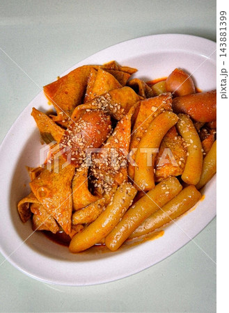 Spicy Korean tteokbokki with chewy rice cakes in a vibrant red sauce, topped with sesame seeds and green onions. A popular street food known for its addictive flavor and satisfying texture. 143881399