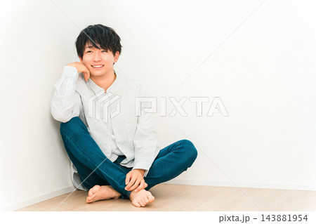 白い壁を背景に床に座って笑顔を見せる若い男性。 白い壁を背景に床に座って笑顔を見せる若い男性。 143881954