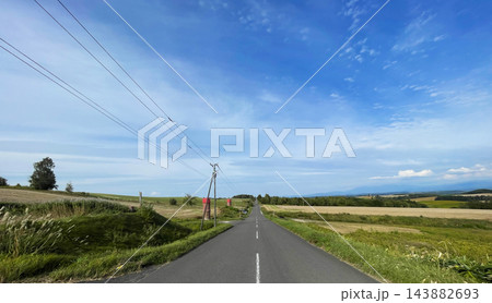 北海道上富良野町・丘陵を走る直線道路とアップダウンの絶景風景 143882693